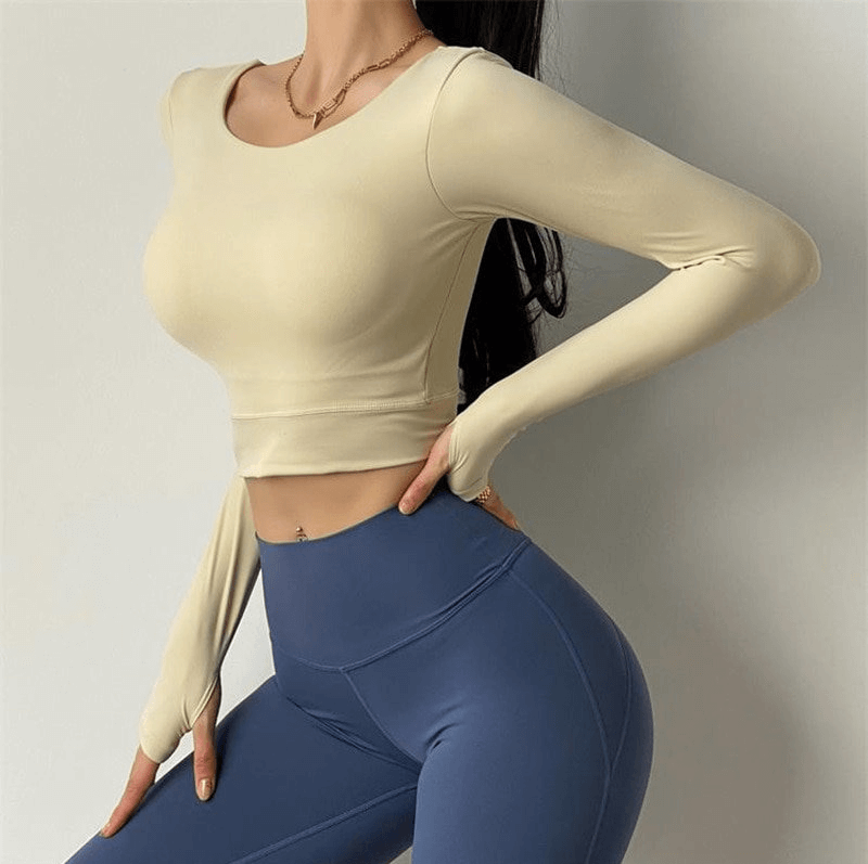 Woman wearing a beige sporty elastic cropped top with long sleeves and open back, paired with blue leggings, perfect for workouts.